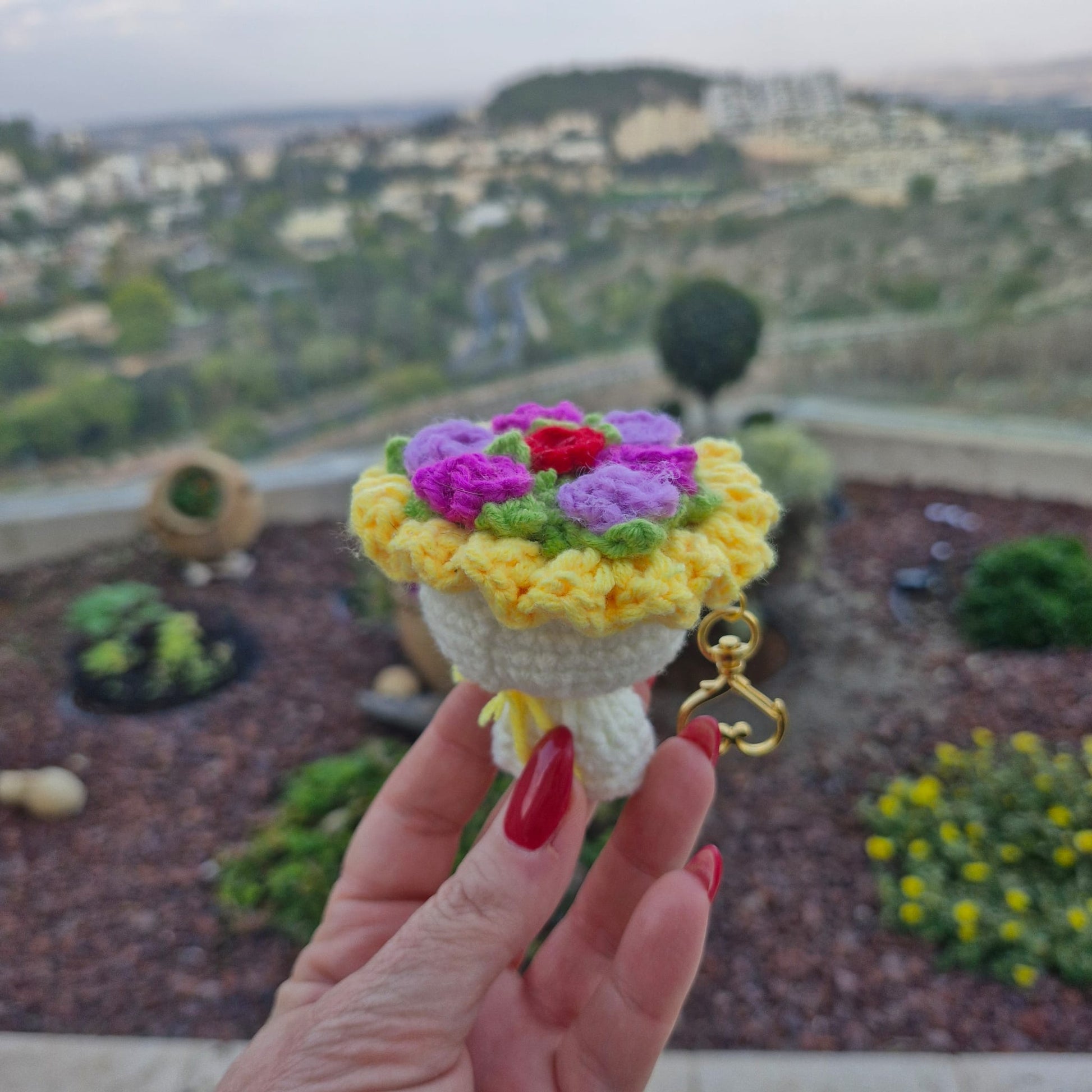 מחזיק מפתחות זר פרחים סרוג בעבודת יד, מוחזק ביד על רקע חוץ מטושטש